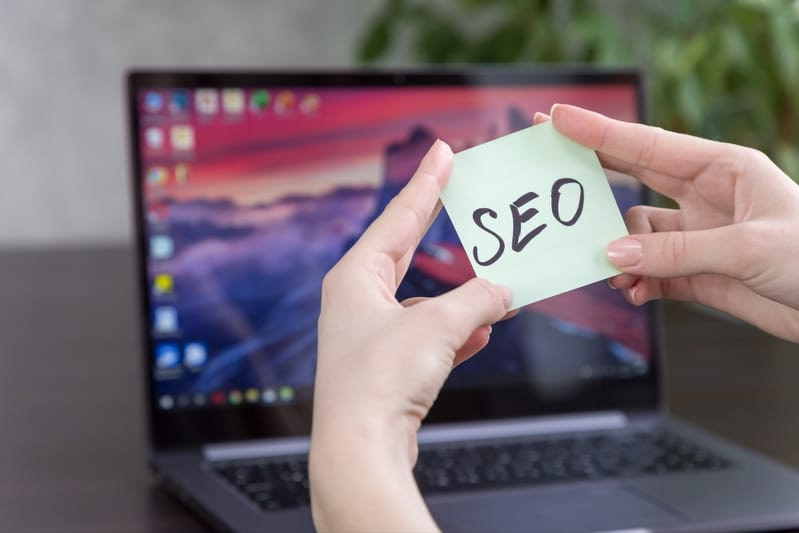 SEO Tips for Ranking a Website - Woman holding a sign saying SEO in front of her laptop